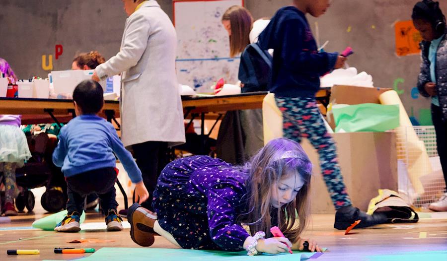 Photo of children at Nottingham Contemporary. A young girl is seen in the foreground colouring on the floor