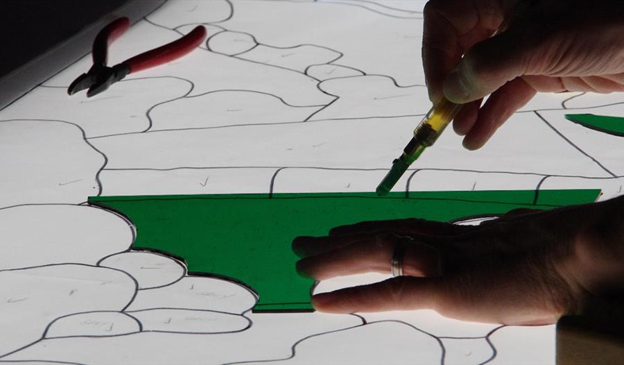 A close up of hands cutting a piece of stained glass