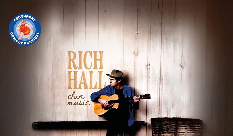 Image of American Comedian Rich Hall sitting down playing the guitar and looking to his right, his name and the name of his show Chin music are writte