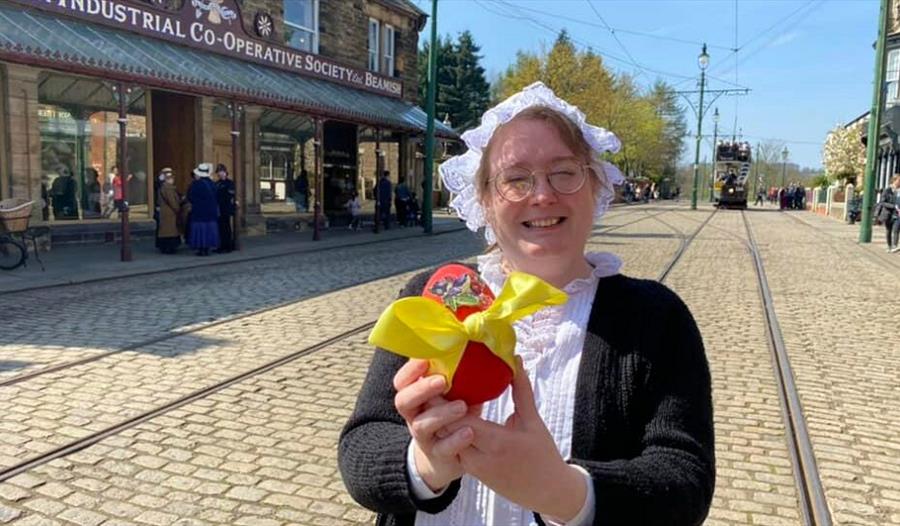 A member of staff in traditional clothing holding an Easter Egg with a yellow bow on it