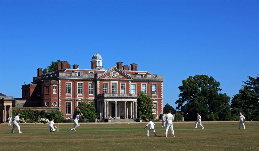 Cricket match taking place on the grounds outside Stansted House