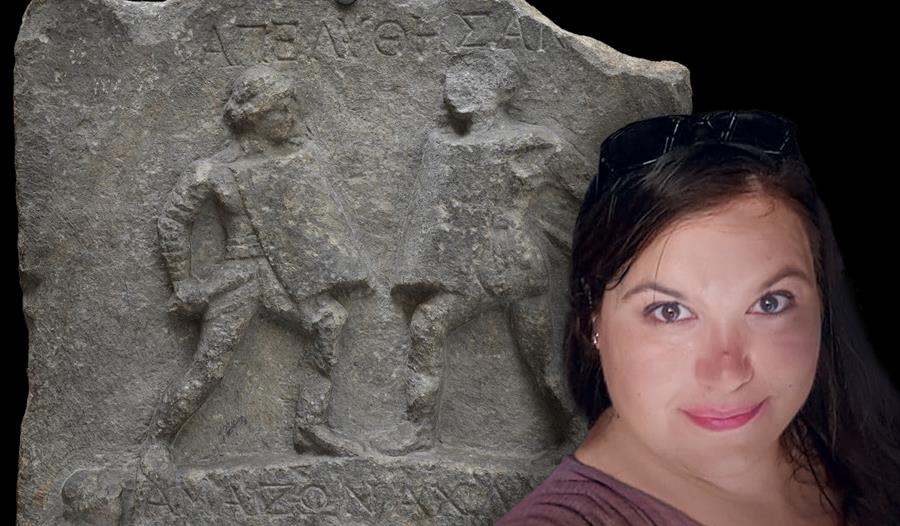 A photograph of Alexandra Sills in front of an image of Amazon and Achillea - the female fighters of Halicarnassus