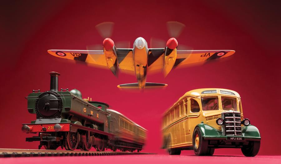 Models of a bus, plane and train against a red background