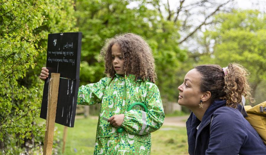 A child and parent looking at a trail sign in a garden.