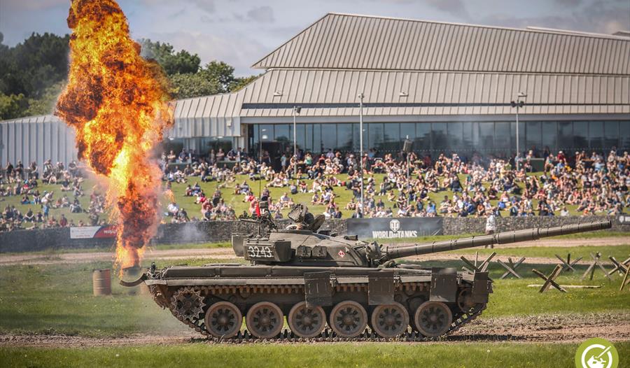 Tank shooting out fire with a crowd of people in the background