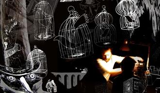 Man in dark room, lit by a warm spotlight from the right, with drawings of birds in cages surronding him.