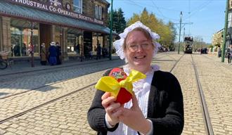 A member of staff in traditional clothing holding an Easter Egg with a yellow bow on it