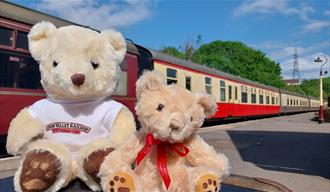 Two teddy bears with a train in the background.