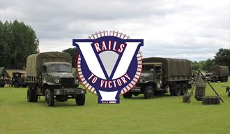 Several classic military vehicles parked in a field, with Rails To Victory branding over the top