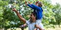A young boy on a man's shoudlers pointing up at the trees