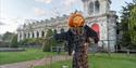 A spooky scarecrow, with a carved pumpkin for a head, in front of the historic Trentham Hall at The Trentham Estate