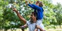 A young boy on a man's shoudlers pointing up at the trees