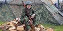 A soldier in WW2 uniform holding a rifle and sitting on a pile of split logs at the Weston-super-Mare Helicopter Museum Military History weekend
