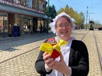 A member of staff in traditional clothing holding an Easter Egg with a yellow bow on it