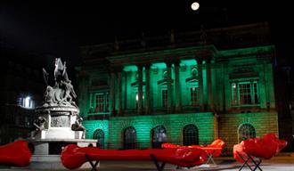 The neoclassical Town Hall is lit in green lighting at night time.