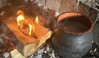 An open fire and a clay pot heating up next to it.