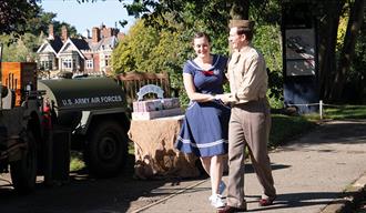 A couple jive dance outside at Bletchley Park. The Bletchley Park Mansion is in view behind them.
