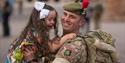 Returning soldier, still in uniform, hugs and lifts up their young daughter, both smiling.