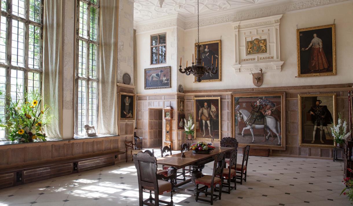 The Great Hall at Parham House. Dining table and chairs in centre of room with large portraits on the wall.