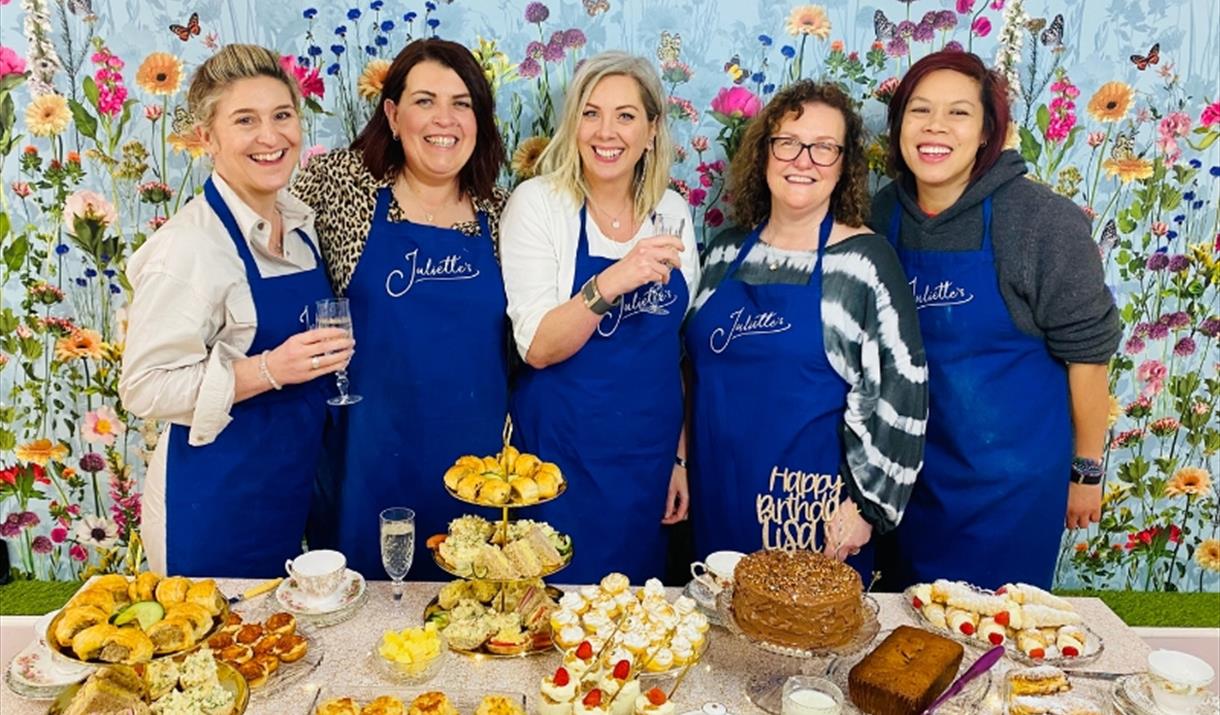 A small group of women stand behind a table display of afternoon tea