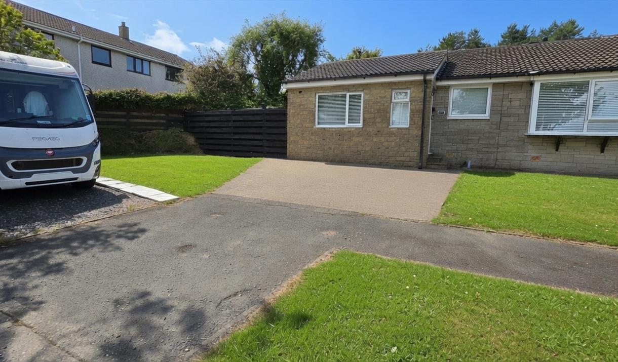 Exterior view of Ballaquark Bungalow with a white motorhome parked on the driveway, green lawn and blue sky.