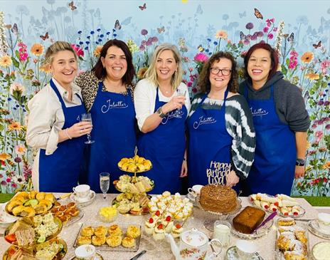 A small group of women stand behind a table display of afternoon tea