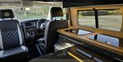 Inside the campervan, sat in the rear looking forward, lights on, table out and front seat swivelled