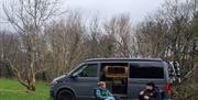 Friends sitting and chatting outside the campervan, using the provided camping accessories at Glen Wyllin Campsite