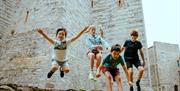 Four children jumping towards the camera in the castle grounds.