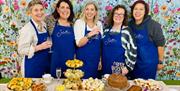 A small group of women stand behind a table display of afternoon tea