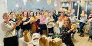 A large group of smiling women hold a bonnag they have baked to the camera