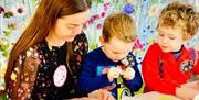 A woman helps two small boys with a craft activity