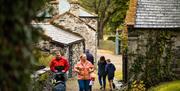 Family group walking between the farm buildings at the Grove. A man is pushing a pram.