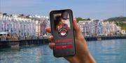 Hand holding a phone with the Go Quest Adventures app on it. Douglas promenade in the background
