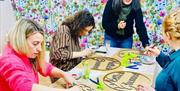A group of women decorate a wooden hoop each that displays the words Nollick Ghennal