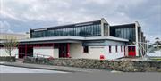Cream coloured swimming pool building with red doors and windows. Glazing over the first floor.