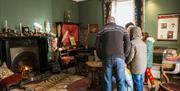 A group of visitors in the sitting room at the Grove. They have their backs to us. The fire is glowing. There is a tiger skin on the floor as a rug.