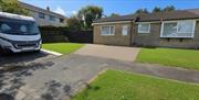 Exterior view of Ballaquark Bungalow with a white motorhome parked on the driveway, green lawn and blue sky.