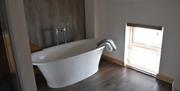 White roll top bath in apartment bathroom with window to Laxey Bay