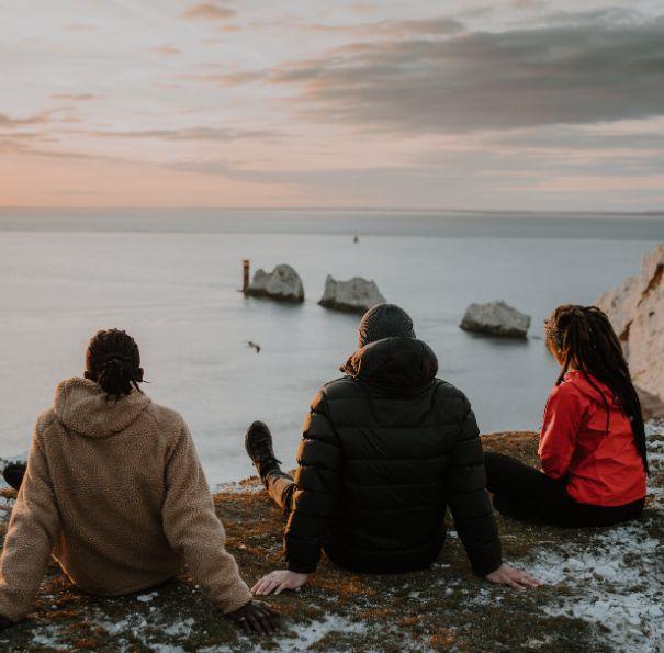 Group of friends sitting on the cliff looking out to sea with a view of the Needles on the Isle of Wight.