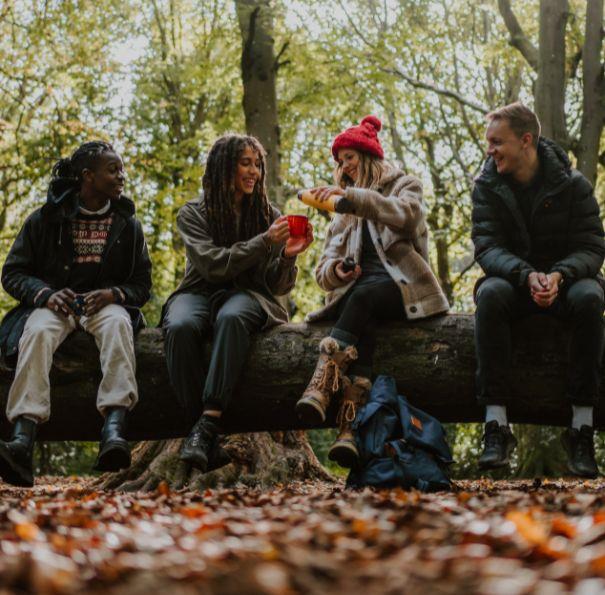 Group of friends sitting on a log in the forest on the Isle of Wight enjoying a hot drink