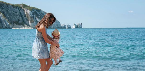 Mother holding daughter on Alum Bay beach with the Needles in the background on the Isle of Wight