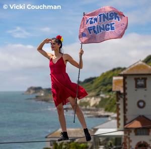 Lady walking along a tightrope with a Ventnor Fringe flag with the sea in the background in Ventnor on the Isle of Wight
