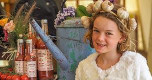 A girl wearing a garlic headband standing next to local produce at the Isle of Wight Garlic Festival, what's on, event