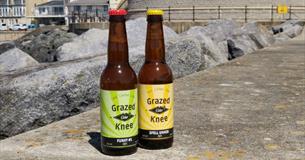 Two bottles of Grazed Knee Cider bottles standing on the walkway at Ventnor Esplanade, Isle of Wight, local producers, local produce, let's buy local