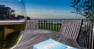 Glass of wine and book on the outside dining tables with sea views at Beach Cottage, Fort Victoria Cottages, Yarmouth, Isle of Wight, self catering