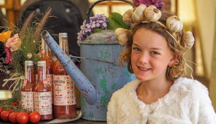 A girl wearing a garlic headband standing next to local produce at the Isle of Wight Garlic Festival, what's on, event