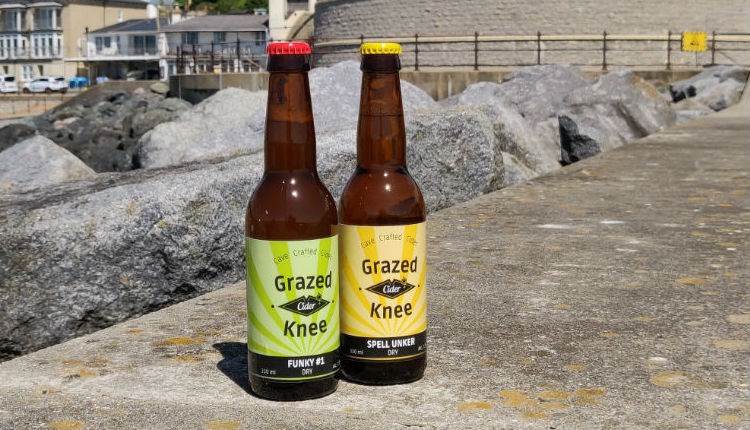 Two bottles of Grazed Knee Cider bottles standing on the walkway at Ventnor Esplanade, Isle of Wight, local producers, local produce, let's buy local