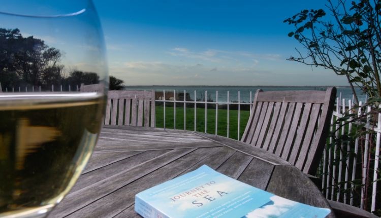 Glass of wine and book on the outside dining tables with sea views at Beach Cottage, Fort Victoria Cottages, Yarmouth, Isle of Wight, self catering