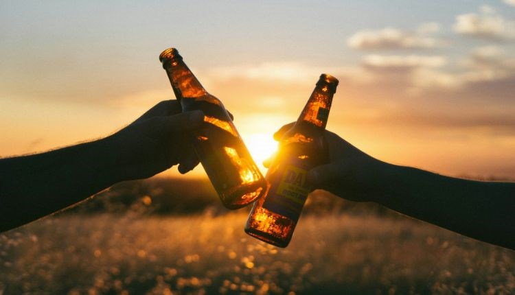Two people clunking two bottles of beer together with a sunset behind, Beer, music and poetry festival at Waverley Park Holiday Centre, Isle of Wight,
